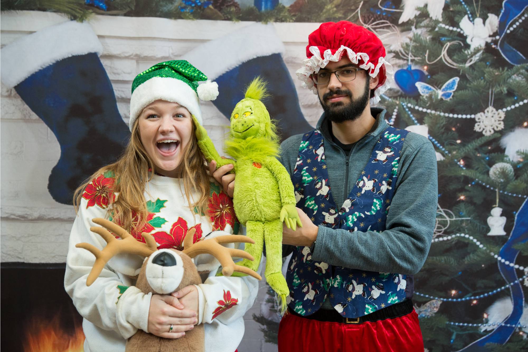 2 GVSU students dressed in Christmas clothes and holding a stuffed grinch and reindeer